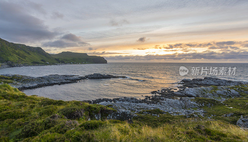 Wonderful sunset above the sea  on Runde island with fresh grass in the foreground and mountains in the background. Runde, Møre og Romsdal, Norway